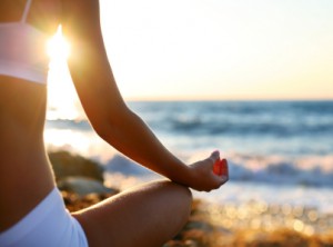 Woman meditating on the beach at sunset.